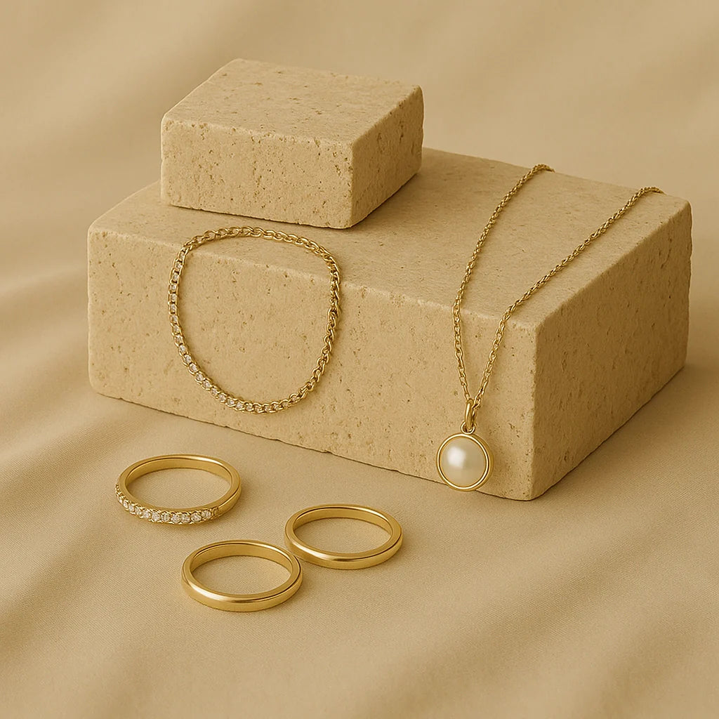 GlamoROZ Jewelry collection featuring gold rings, a delicate chain bracelet, and a pearl pendant necklace displayed on neutral stone blocks.