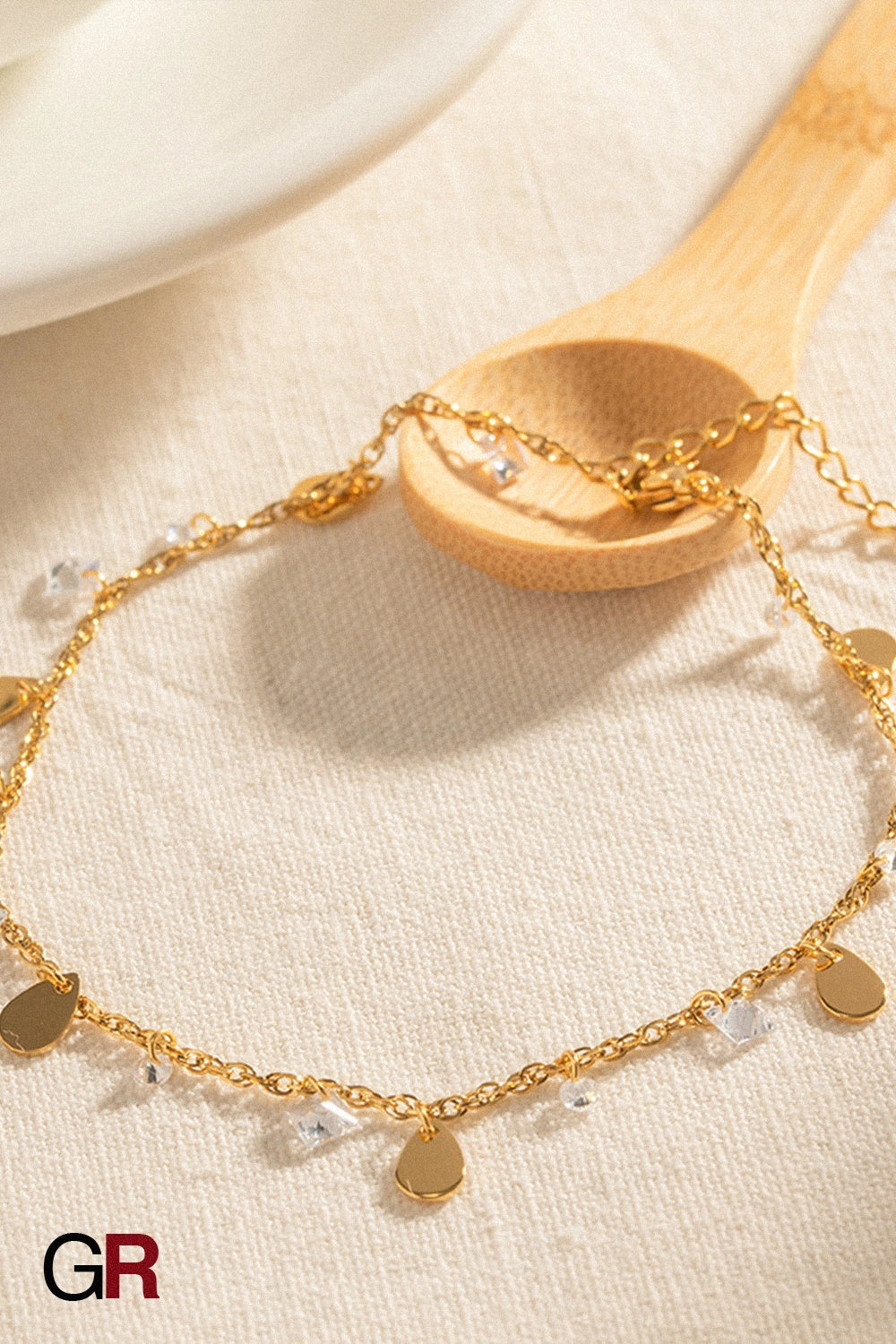 “GlamoROZ Éclat Doré Luminous Tassel Anklet flat-lay on soft beige fabric background”