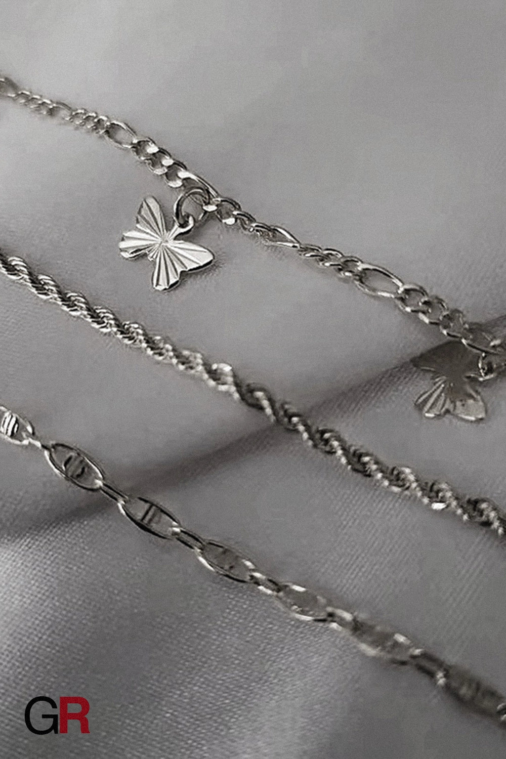 “GlamoROZ Jardin Papillon Golden Anklet Set layered flat-lay with other GlamoROZ jewelry on beige fabric background”